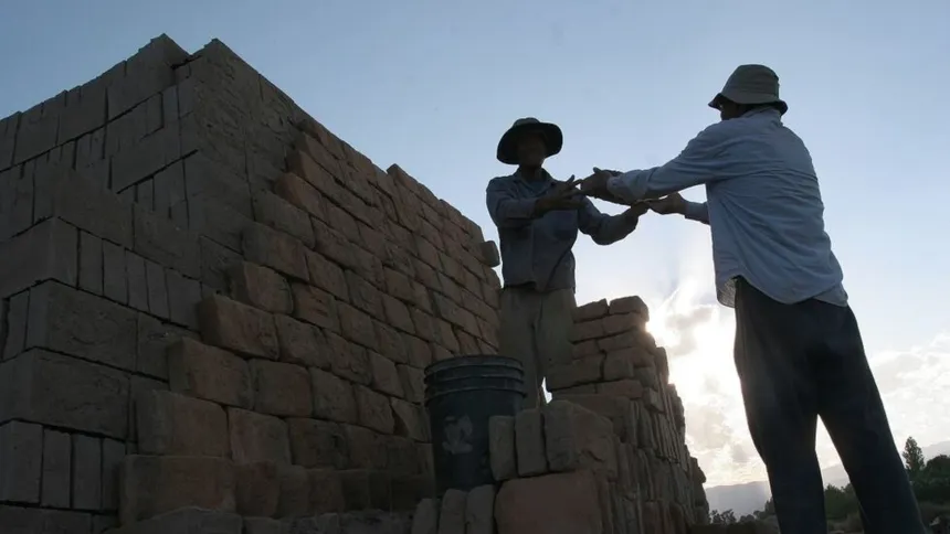 Dos trabajadores construyen una pared de ladrillos al aire libre.