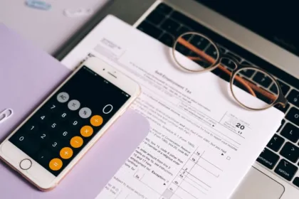 Formulario de impuestos, calculadora y anteojos sobre una computadora portátil.