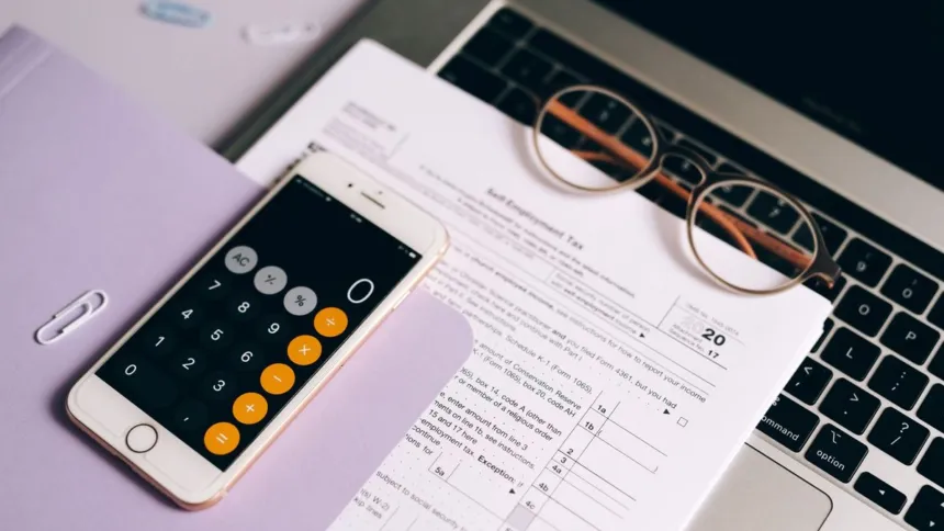 Formulario de impuestos, calculadora y anteojos sobre una computadora portátil.