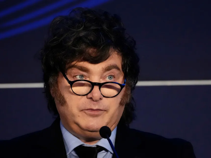 Javier Milei, con anteojos, habla ante un micrófono.