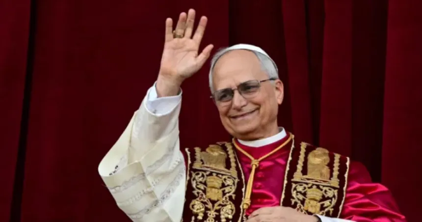 El papa León XIV saluda con la mano frente a una cortina roja.