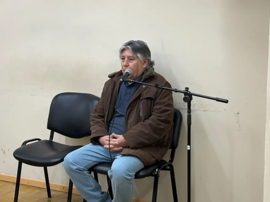 Un hombre sentado frente a un micrófono en una sala.