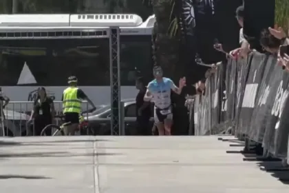 Un triatleta llega a la meta entre vallas y espectadores.