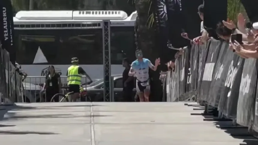 Un triatleta llega a la meta entre vallas y espectadores.