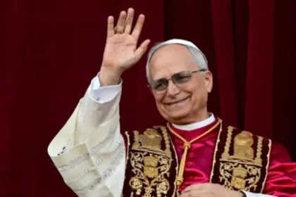El papa León XIV saluda con la mano frente a una cortina roja.