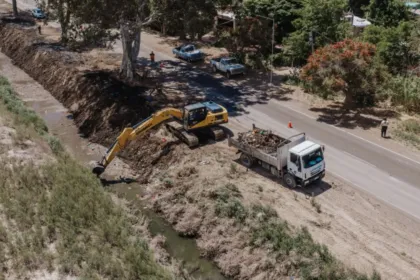 Una excavadora limpia un desagüe junto a una ruta y un camión carga los sedimentos.