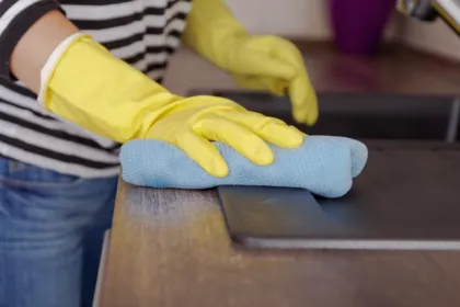 Una persona con guantes amarillos limpia una superficie con un paño azul.