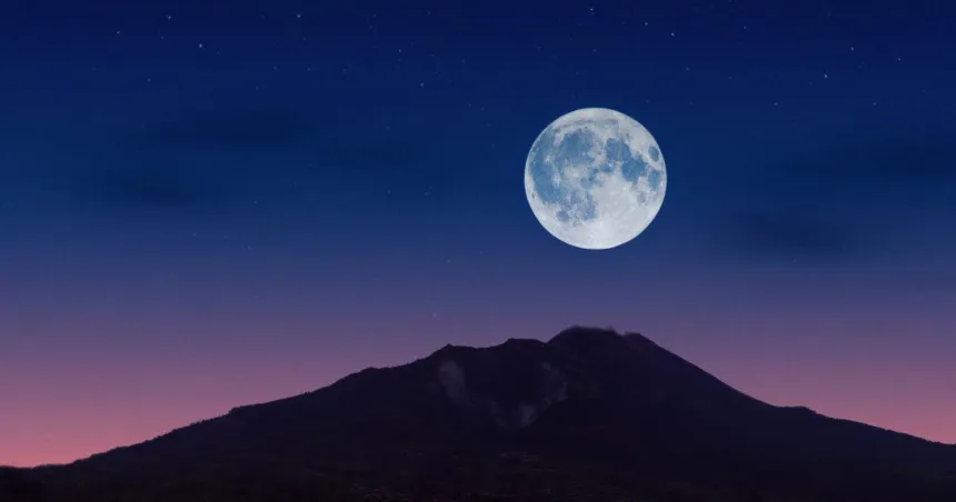 Luna llena sobre una montaña bajo el cielo del atardecer.