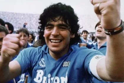 Diego Maradona sonríe con la camiseta del Napoli y levanta los brazos entre hinchas.