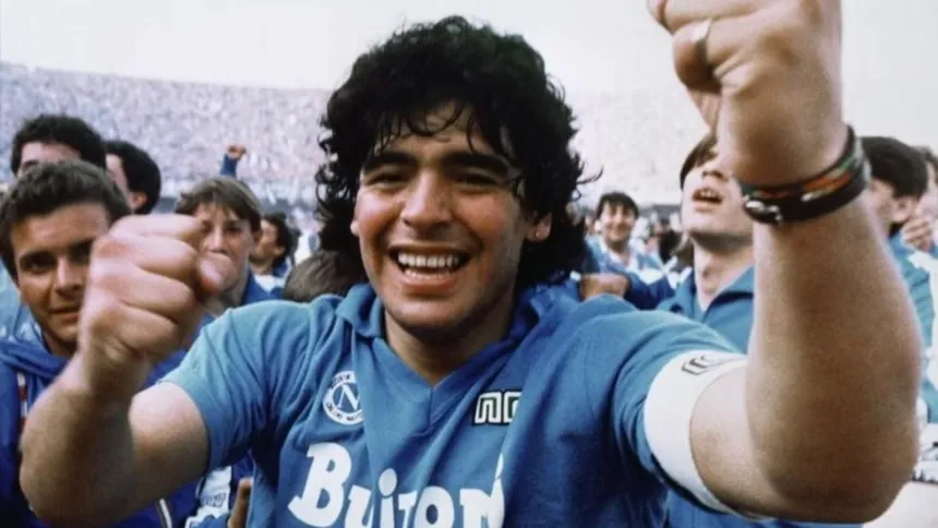Diego Maradona sonríe con la camiseta del Napoli y levanta los brazos entre hinchas.