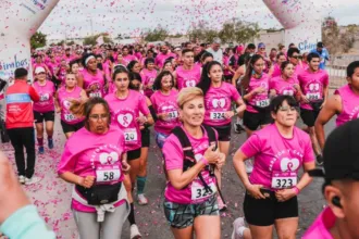 Participantes con remeras rosas corren bajo un arco en una maratón contra el cáncer de mama.