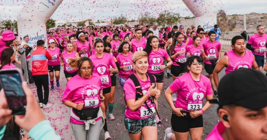 Participantes con remeras rosas corren bajo un arco en una maratón contra el cáncer de mama.