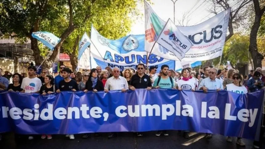 Docentes, nodocentes y estudiantes marchan en San Juan detrás de una bandera que dice Presidente, cumpla la ley.