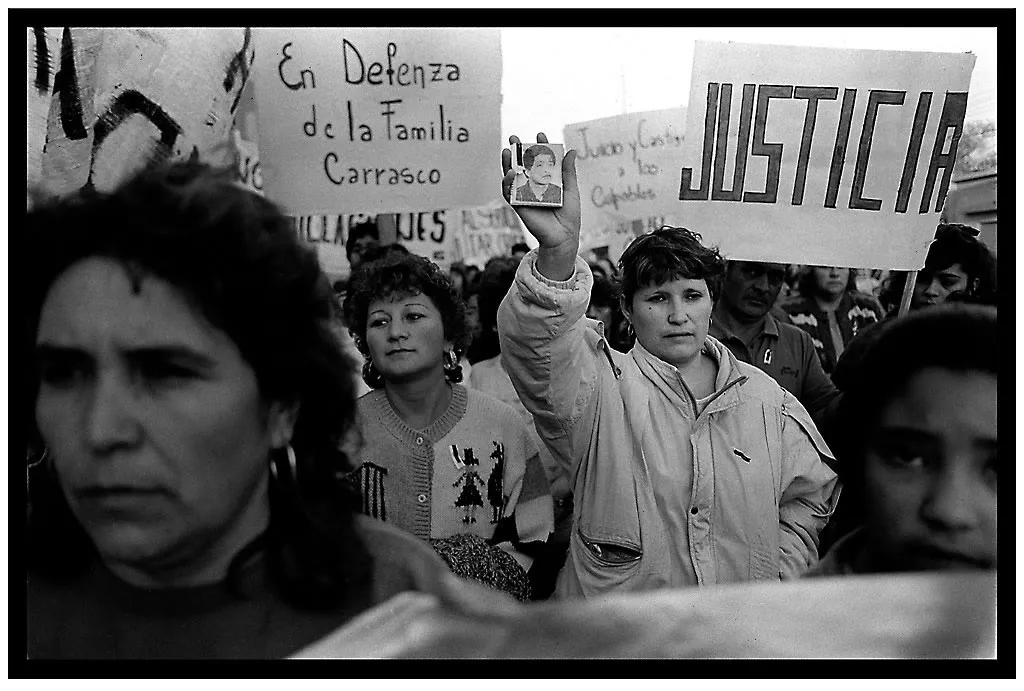 Foto en blanco y negro de una marcha: mujeres con carteles que dicen «En defensa de la familia Carrasco» y «Justicia».