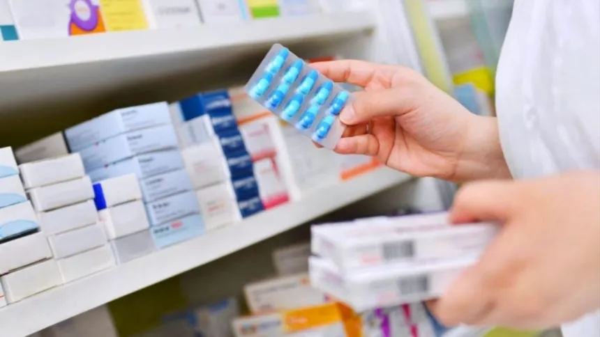 Una persona sostiene un blíster de pastillas frente a estantes de medicamentos.