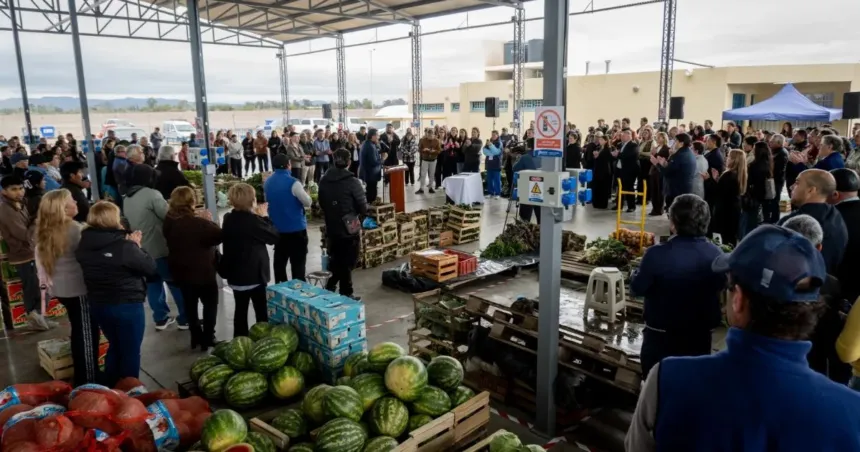 Personas reunidas entre cajones de frutas y verduras en un mercado cubierto.