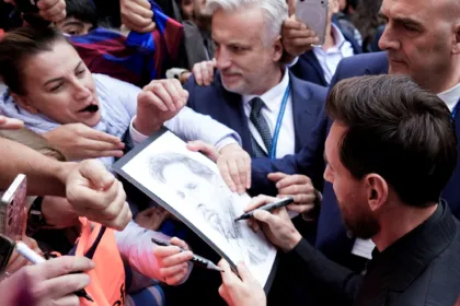 Messi firma un dibujo rodeado de personas que le piden autógrafos.