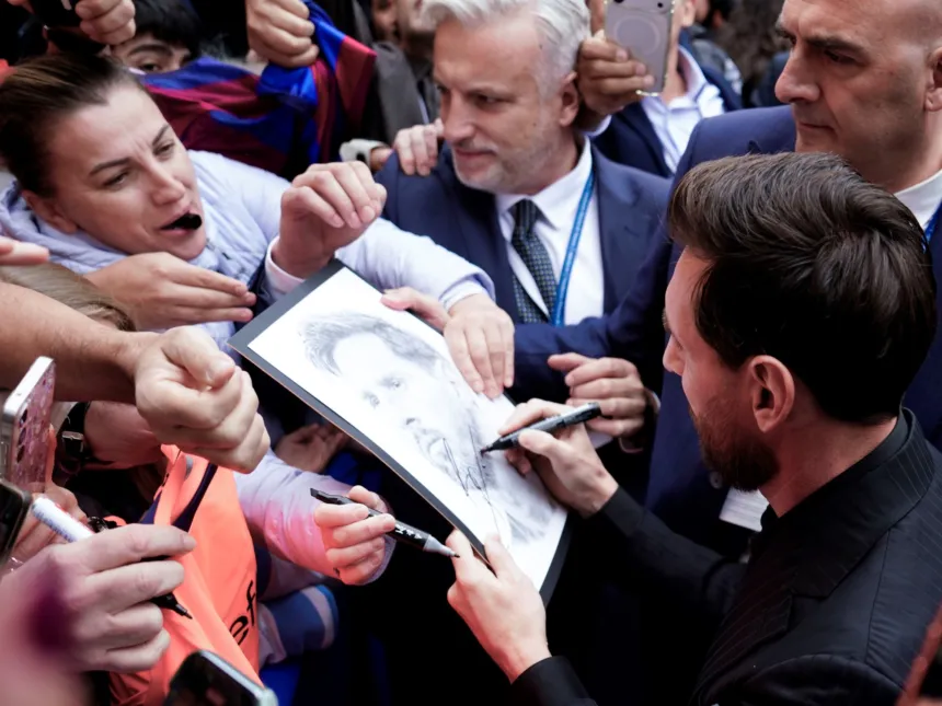 Messi firma un dibujo rodeado de personas que le piden autógrafos.