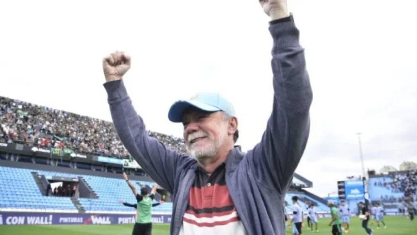 Un hombre con gorra levanta los brazos en una cancha de fútbol.