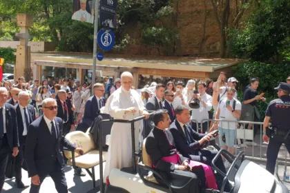 El papa León XIV, de blanco y de pie en un vehículo descubierto, saluda a la gente que lo espera detrás de las vallas en Montserrat, en junio.