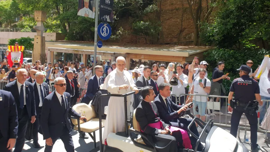 El papa León XIV, de blanco y de pie en un vehículo descubierto, saluda a la gente que lo espera detrás de las vallas en Montserrat, en junio.