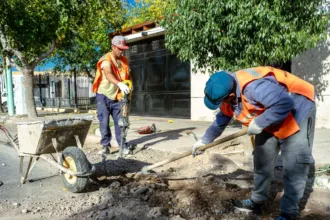 Dos trabajadores con chalecos reflectantes reparan una vereda.