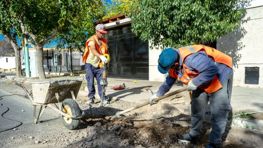 Dos trabajadores con chalecos reflectantes reparan una vereda.