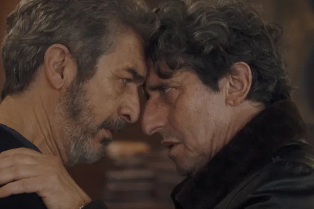 Dos hombres adultos se miran de cerca en una escena de ficción.