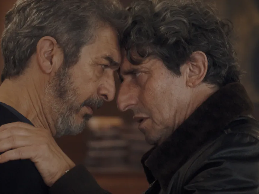 Dos hombres adultos se miran de cerca en una escena de ficción.