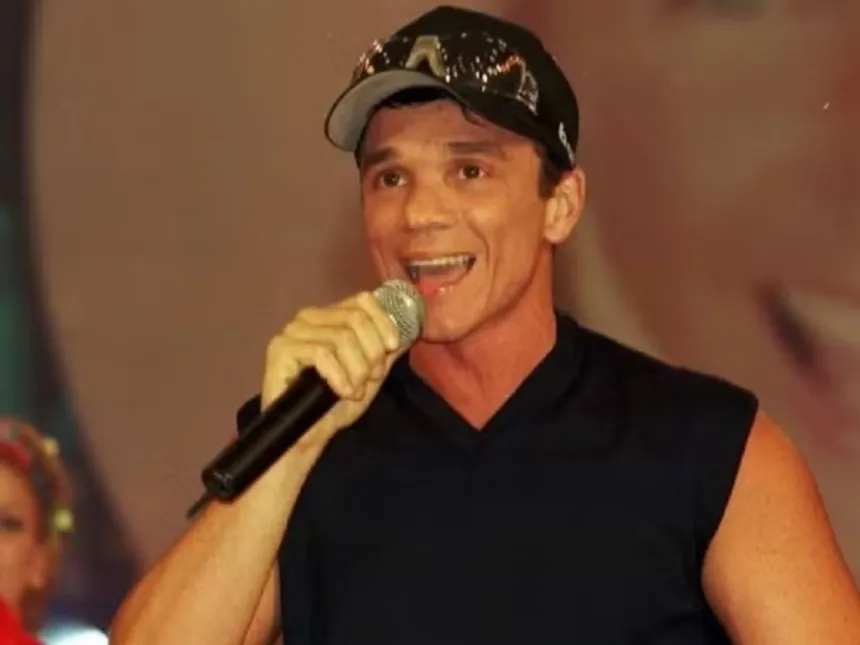 Un cantante con gorra canta sosteniendo un micrófono.