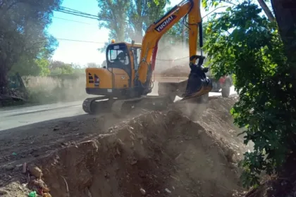 Una excavadora trabaja sobre un montículo de tierra junto a un camino.