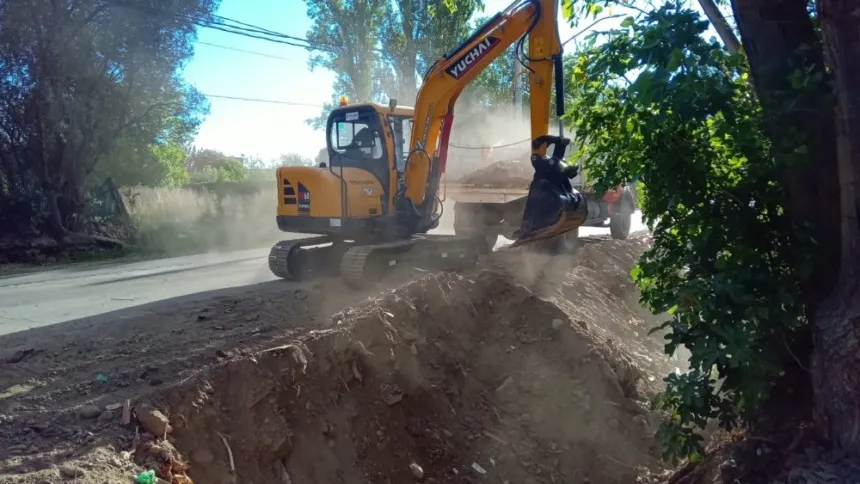 Una excavadora trabaja sobre un montículo de tierra junto a un camino.