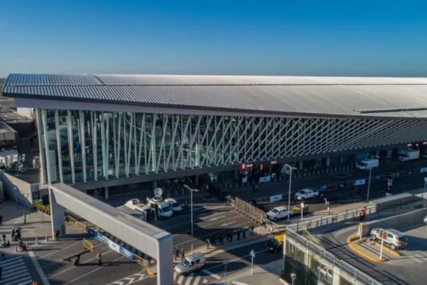 Vista aérea de una terminal aeroportuaria con vehículos y pasajeros en el acceso.
