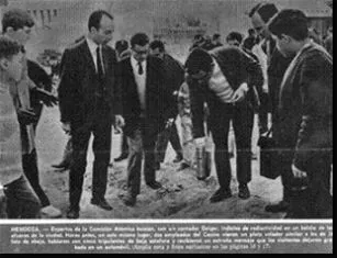 Foto en blanco y negro: un grupo de hombres de traje rodea a otro que, inclinado sobre la tierra de un baldío, sostiene un aparato de medición. Abajo, un epígrafe impreso.