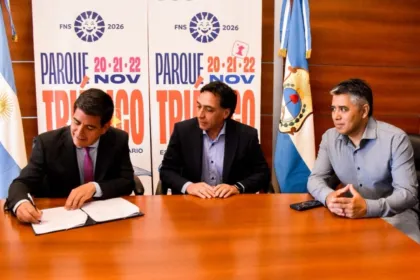 Tres hombres firman un acuerdo con carteles de la Fiesta Nacional del Sol 2026 al fondo.