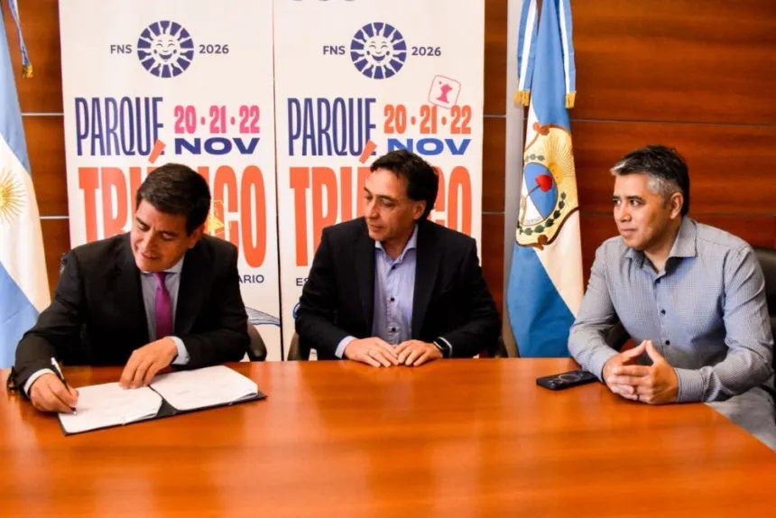 Tres hombres firman un acuerdo con carteles de la Fiesta Nacional del Sol 2026 al fondo.