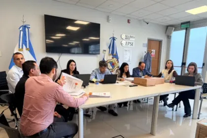 Personas revisan documentos y computadoras durante una reunión en una sala con banderas.