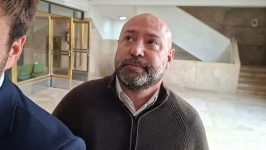 Un hombre adulto con barba está de pie en el interior de un edificio.