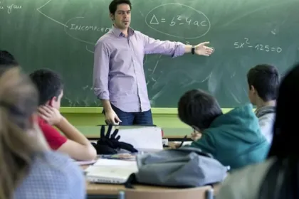Un docente enseña Matemática frente al pizarrón a un grupo de estudiantes.