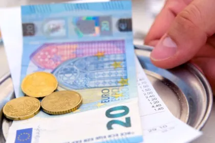 Monedas y un billete de euro sobre una bandeja junto a la cuenta de un restaurante.