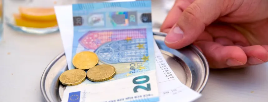Monedas y un billete de euro sobre una bandeja junto a la cuenta de un restaurante.