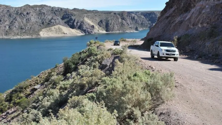 Ruta de ripio junto al agua en el Cañón del Atuel, con dos camionetas.
