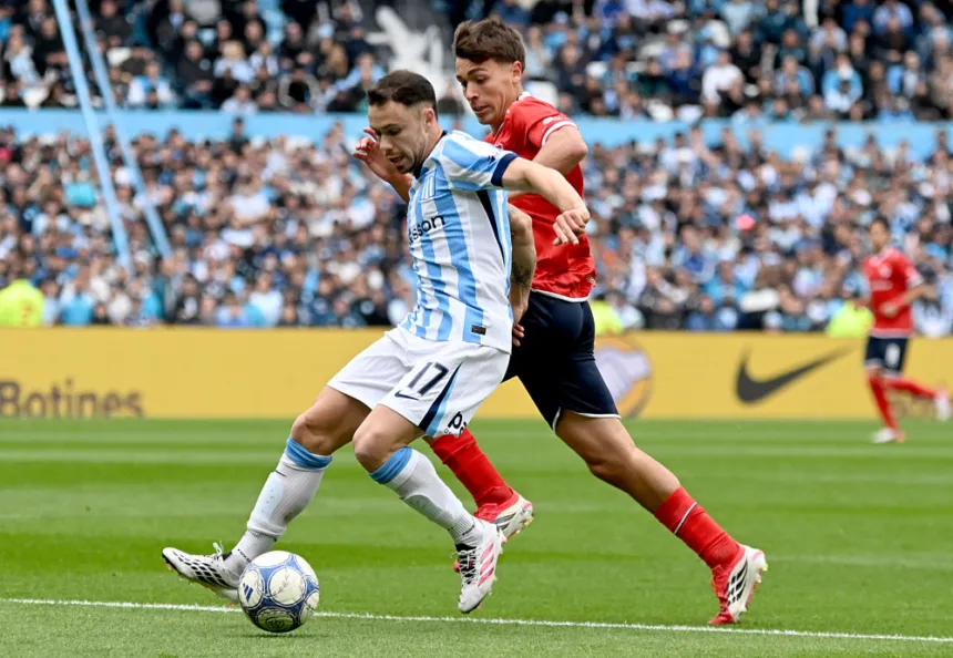 Un jugador de Racing conduce la pelota mientras lo marca un futbolista de Independiente.