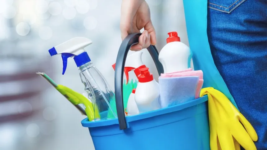 Una persona lleva un balde con productos de limpieza y guantes.