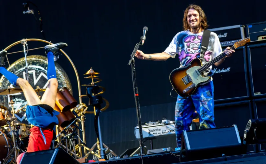 Red Hot Chili Peppers en vivo: Flea hace una vertical junto a la batería mientras John Frusciante toca la guitarra.