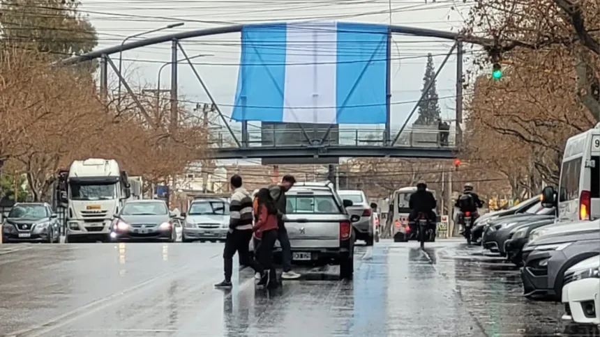 Personas y vehículos circulan por una calle mojada bajo la lluvia.
