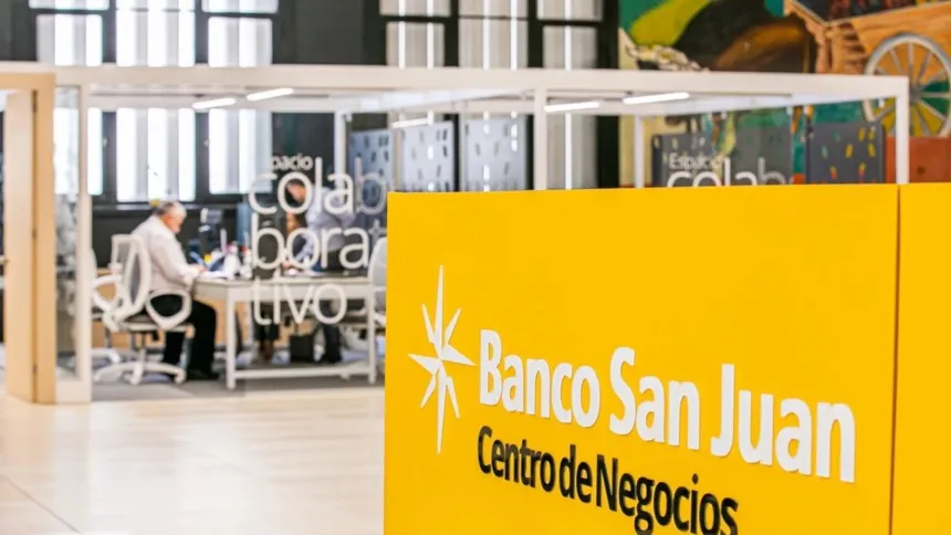 Cartel de Banco San Juan en un centro de negocios, con una persona trabajando al fondo.