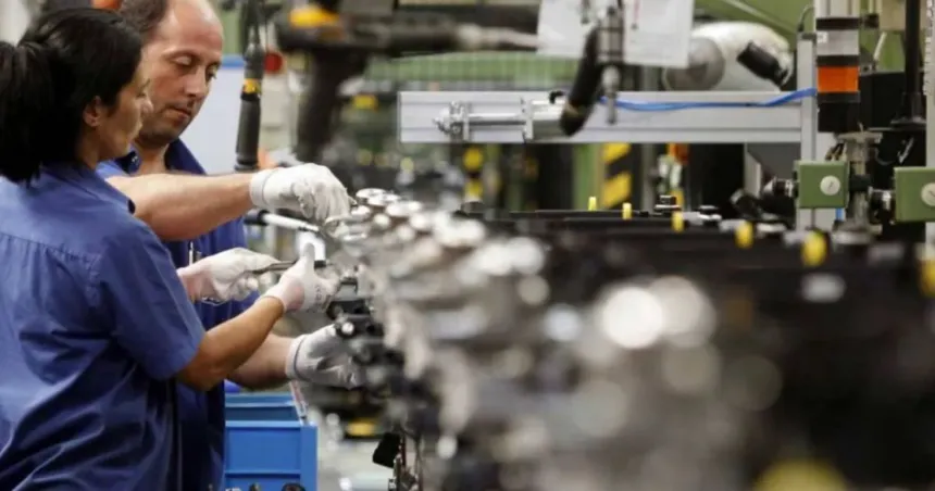 Dos trabajadores con guantes operan maquinaria en una fábrica.