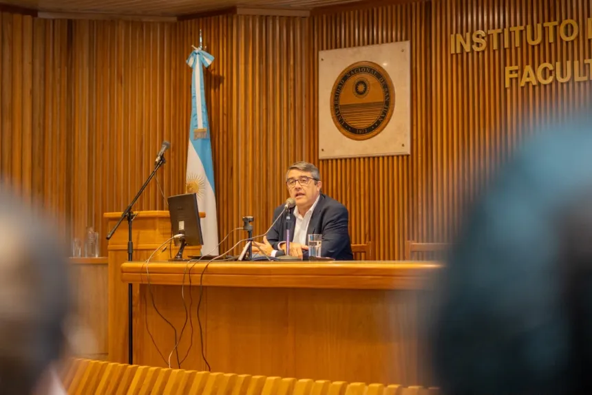 Un funcionario expone desde una mesa en un auditorio universitario.