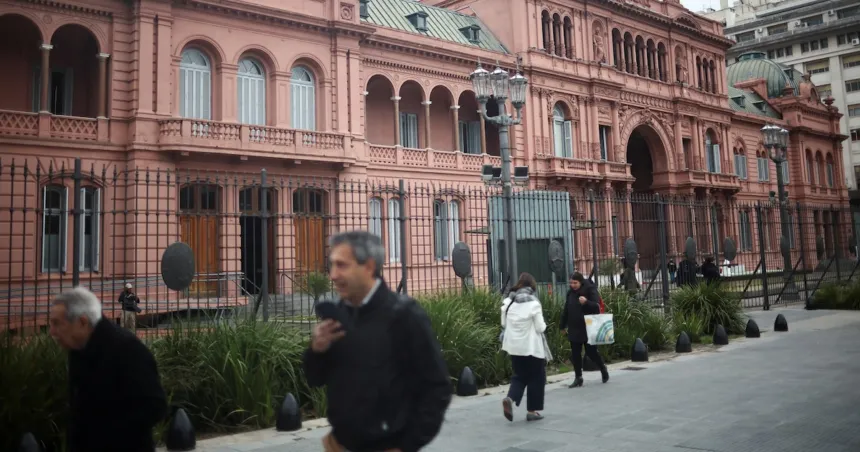 La Casa Rosada vista desde la calle, con peatones caminando frente a sus rejas.